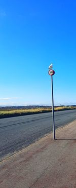 Road sign on field against clear blue sky