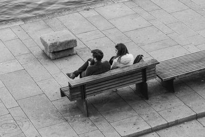 High angle view of couple sitting on bench by lake