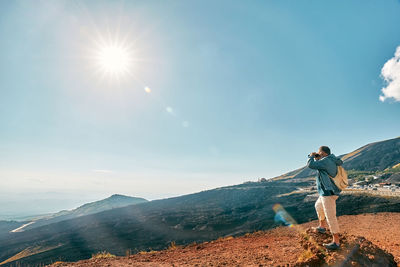 Rear view of man standing on mountain against sky during sunset