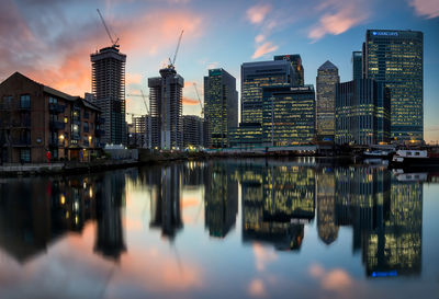 Reflection of buildings in river against sky during sunset
