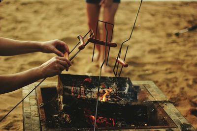 Cropped hand placing sausages on string over barbecue