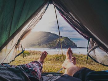 Low section of people lying in tent against mountain and sea