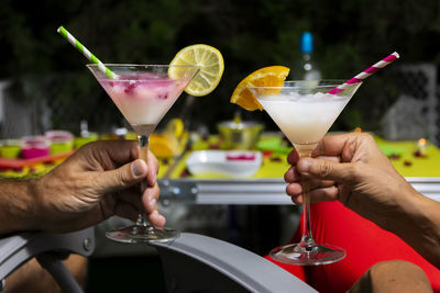 Happy romantic couple celebrating, holding glasses of cocktails with fruits and drinking straws. 