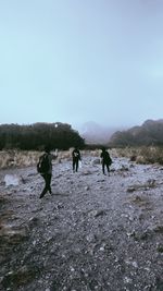 Rear view of people walking on field against sky