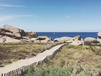 Walkway leading towards beach against sky on sunny day