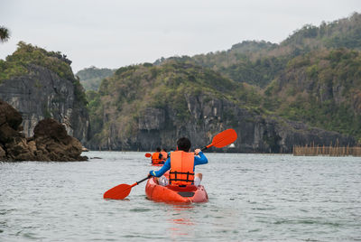 Rear view of man kayaking in lake against sky