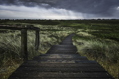 Boardwalk leading towards landscape against sky