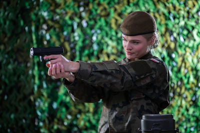 The lady soldier aims her pistol at a distant target, concentrating hard while doing so.