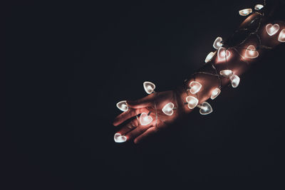 Close-up of illuminated heart shaped lights wrapped on hand against black background