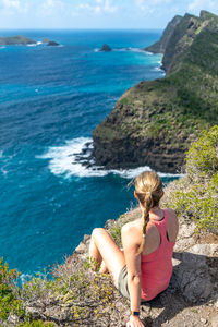 Rear view of woman sitting on rock by sea