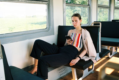 Full length of young woman using phone while sitting in bus