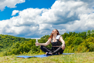 Young woman sitting on field against sky
