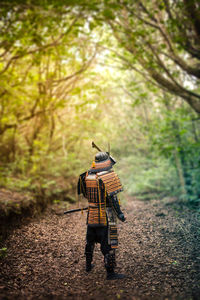 Rear view of man wearing samurai costume amidst trees in forest