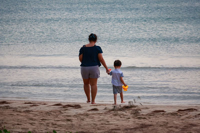 Mother and son walking on shore against sea at beach