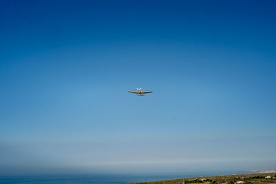 Airplane flying over sea against clear blue sky