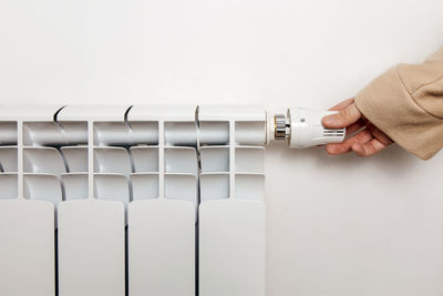 White heating radiator hanging on white wall, close up view. person turns on or turns off radiator.