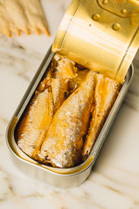 Open tin of sardines packed in olive oil on marble