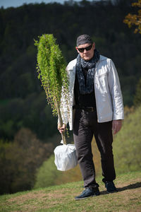 Full length of man holding plant while standing on field
