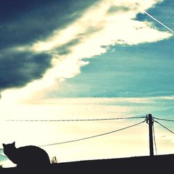 Low angle view of electricity pylon against cloudy sky