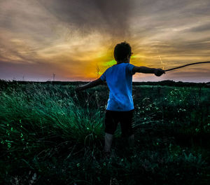 Rear view of man standing on field against sky during sunset