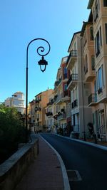 Road leading towards buildings against clear blue sky