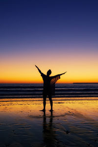 Silhouette people standing on beach against sky during sunset