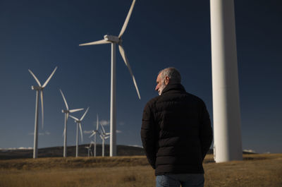 Adult man in winter cloth with modern windmills against blue sky. shot in castilla la mancha, spain