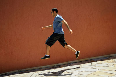 Side view of man levitating over sidewalk by wall