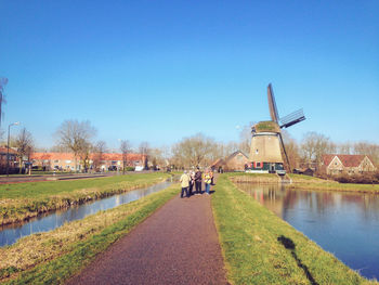 People on footpath by canal against clear sky