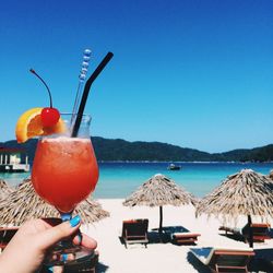 Cropped image of woman holding drink at beach against sky