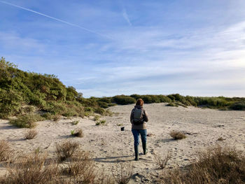 Rear view of man walking on field against sky