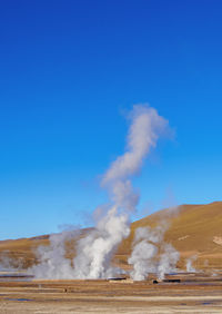 Smoke emitting from volcanic landscape against clear blue sky