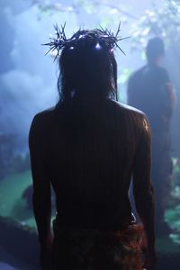 Rear view of man acting as jesus christ with string lights on thorn crown