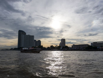 Boats sailing on sea by buildings against sky in city