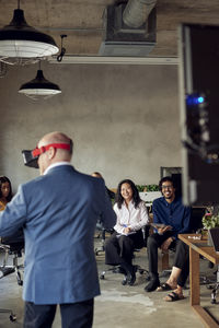 Smiling colleagues looking at mature businessman wearing vr in office