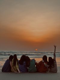 Rear view of people at beach against sky during sunset