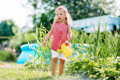 A charming baby is watering a strawberry bush in the garden from a children's toy watering can. 