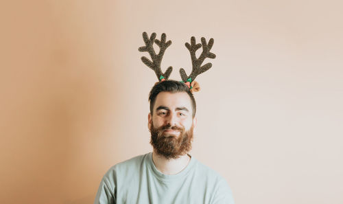 Portrait of young man wearing deer antlers against wall