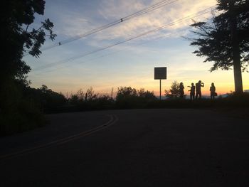 Road by silhouette trees against sky during sunset