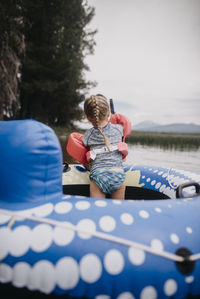 Rear view of girl with water wings standing in inflatable raft on lake