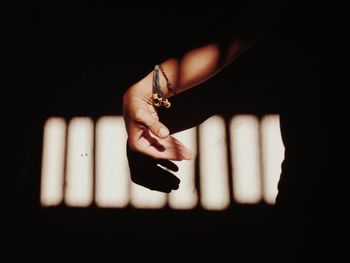 Midsection of person gesturing while sunlight falling on wall
