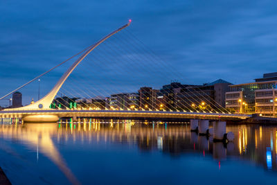 Illuminated bridge over river against cloudy sky