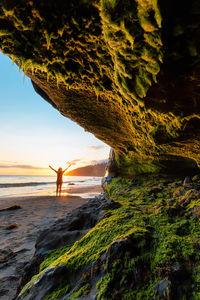 Man standing on rock by sea against sky