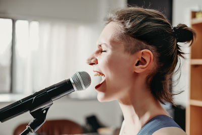 Young emotional woman singing into a microphone. female rock singer on a rehearsal in record studio. 