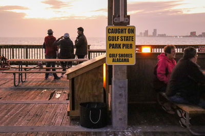 Rear view of people on railing against sea during sunset