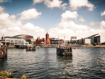 Buildings by river and sea against cloudy sky in city with vintage look and reflections