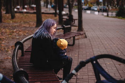 Young mother holding baby son while sitting on bench in park