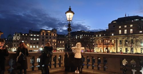 People standing on street against illuminated buildings in city