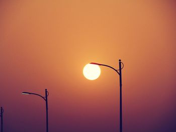 Low angle view of silhouette street lights against orange sky during sunset