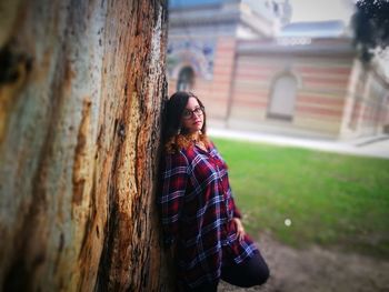 Portrait of smiling young woman against tree trunk